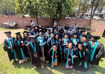 Large group of graduates smiling together in caps and gowns on green lawn.
