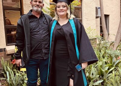 Graduate in gown posing with a man in casual clothes outside a building.