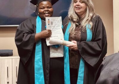Graduate holding certificate with woman during indoor graduation ceremony.