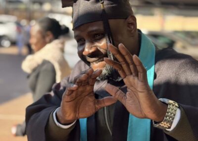 Male graduate posing with hands up in playful gesture outdoors.