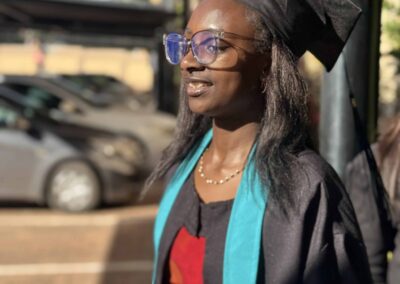 Female graduate in glasses and gown standing in parking area.