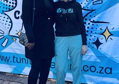 Two women posing in front of a Tuniti Care Hero event banner.