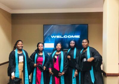 Group of five graduates posing in front of welcome screen at ceremony.