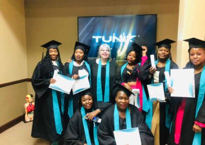 Graduates celebrating indoors with certificates and smiling for a group photo.