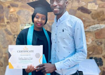 Graduate holding certificate while standing with smiling man by stone wall.