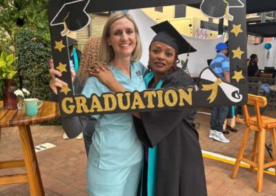 Graduate and woman posing through decorative graduation frame outdoors.