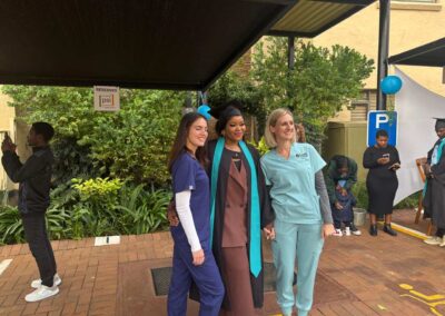 Three women smiling and posing for photo at outdoor event under canopy.