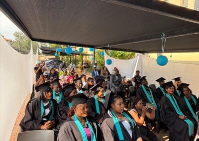 Graduates and staff smiling at event under canopy with Tuniti signage.