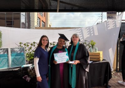 Graduate holding certificate and smiling at outdoor Tuniti celebration.