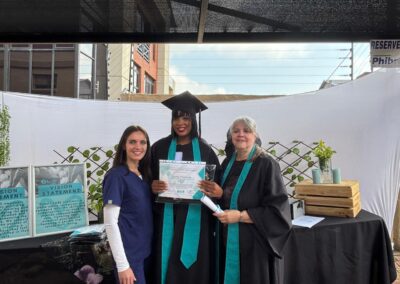 Graduate holding certificate and smiling at outdoor Tuniti celebration.