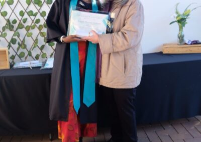 Two women posing in a graduation frame with green field in the background.