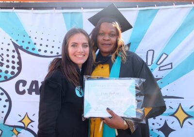 Caregiver graduate proudly holding certificate with mentor, celebrating achievement at caregiver training graduation event with a vibrant comic-style backdrop.