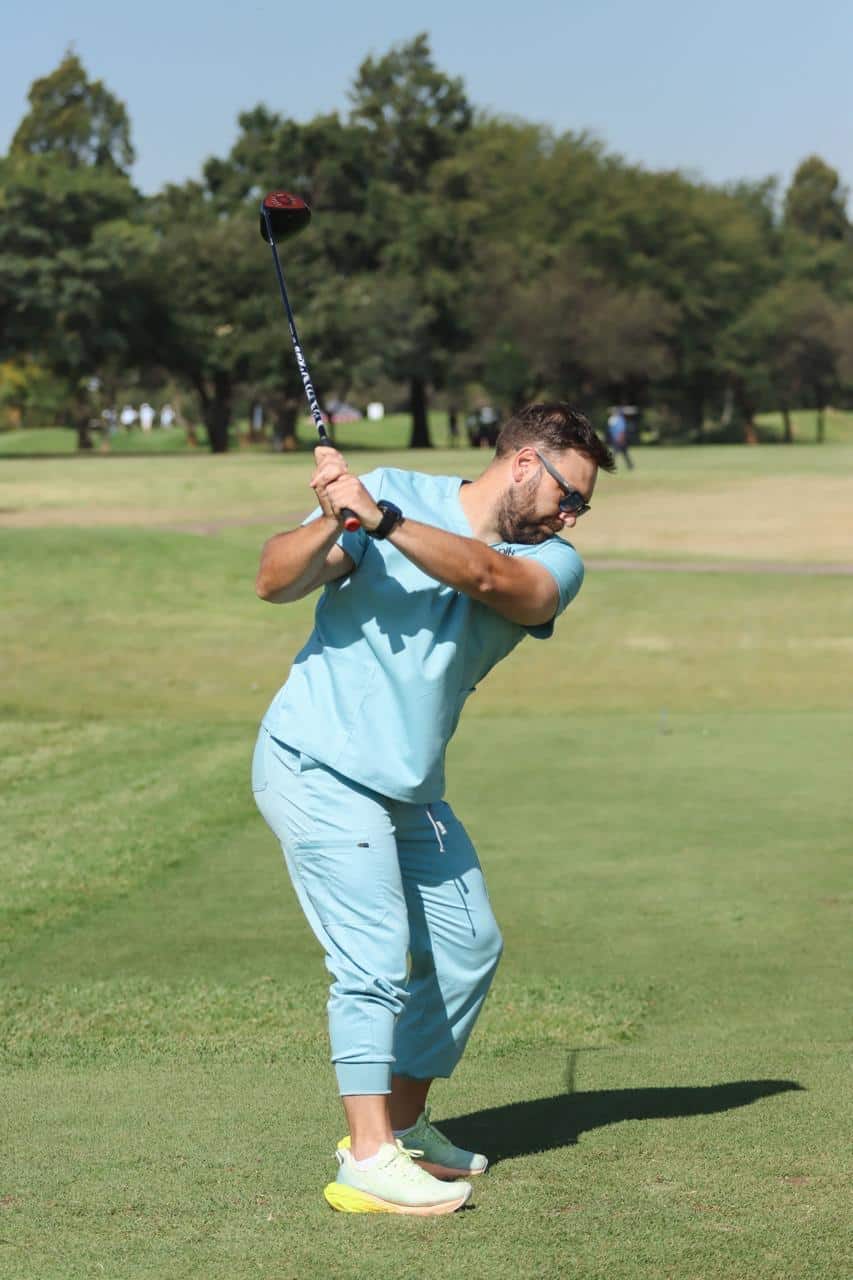 Man swinging a golf club on a sunny day, wearing casual athletic wear on a green golf course, showcasing recreational sports and outdoor wellness.