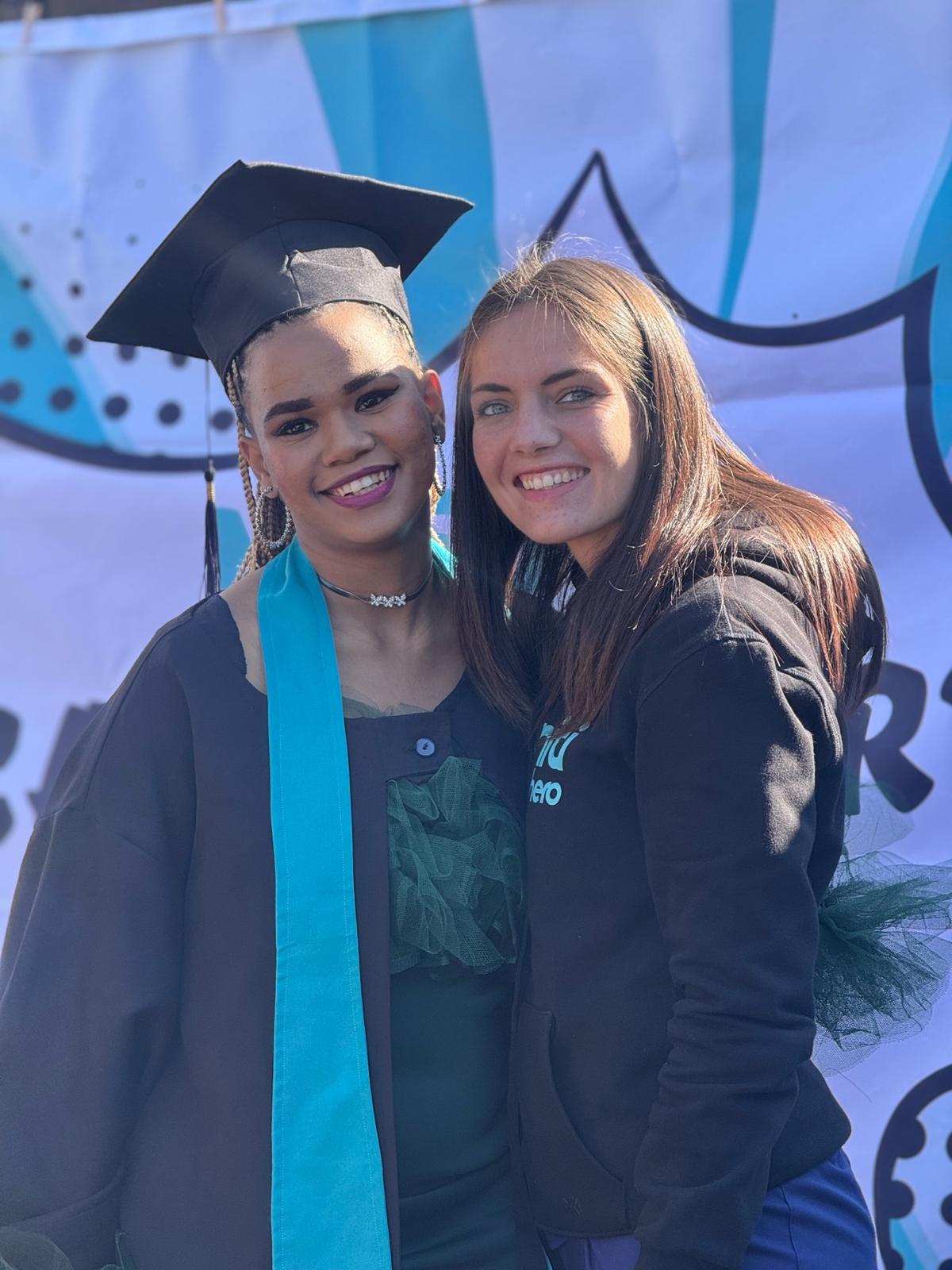 image12 Graduating caregiver in cap and gown poses proudly with a Tuniti Care Hero team member in front of a celebratory backdrop.