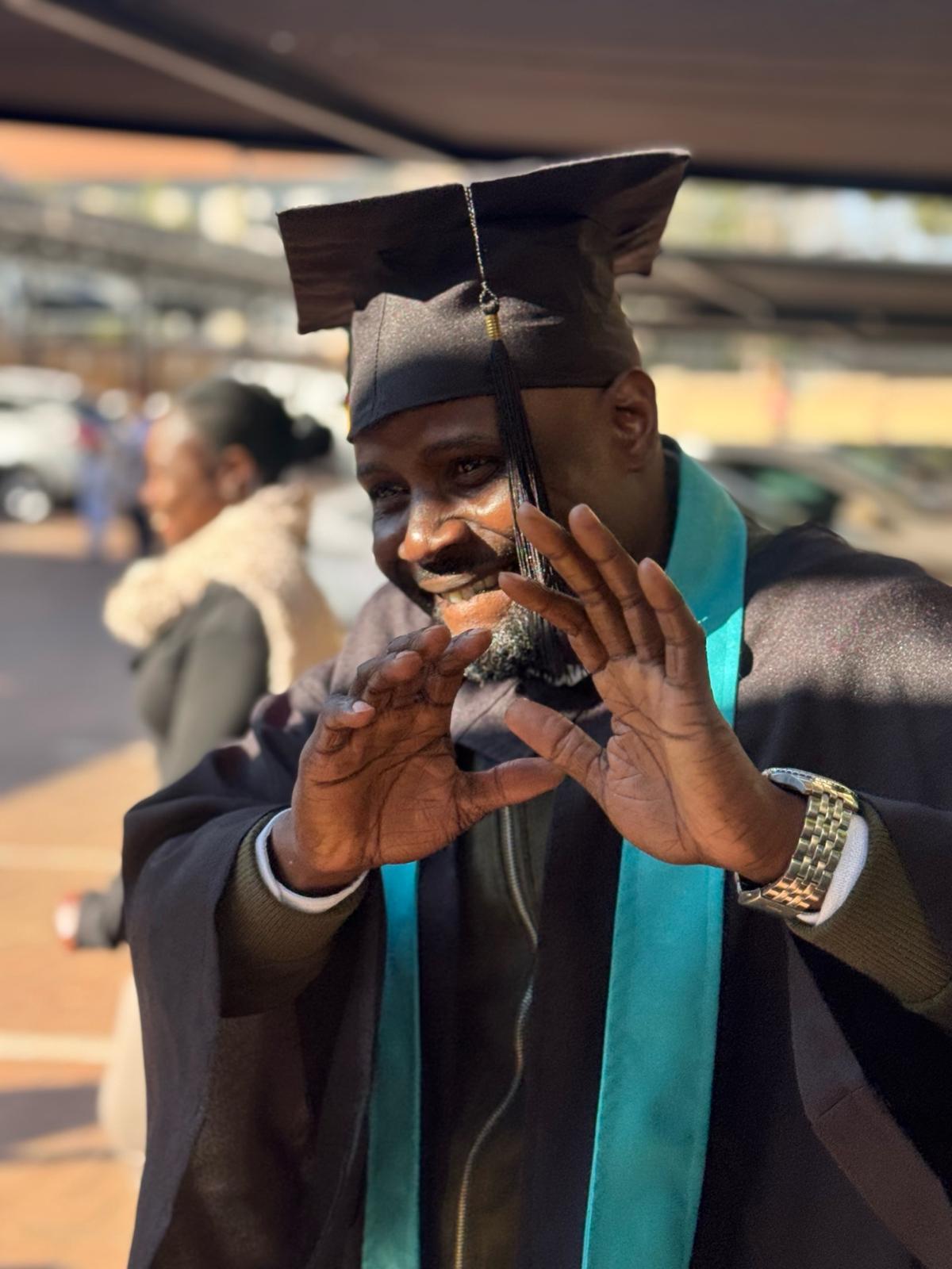 image3 Joyful male graduate in cap and gown making heart shape with hands at Tuniti Care Hero 2025 caregiver graduation event.