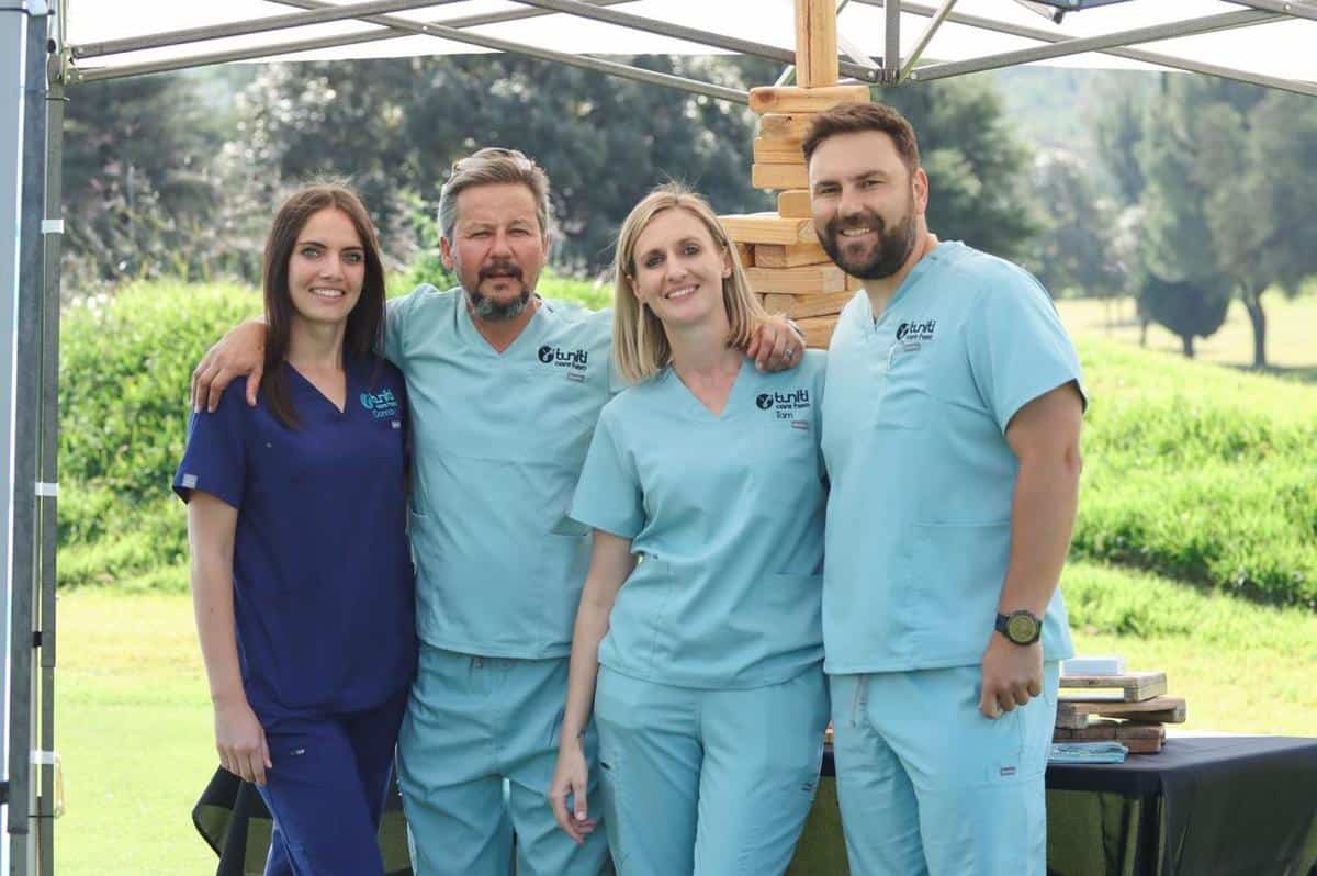 Group of Tuniti Care Hero team members smiling outdoors in branded scrubs, showcasing caregiver community, teamwork, and compassionate healthcare support