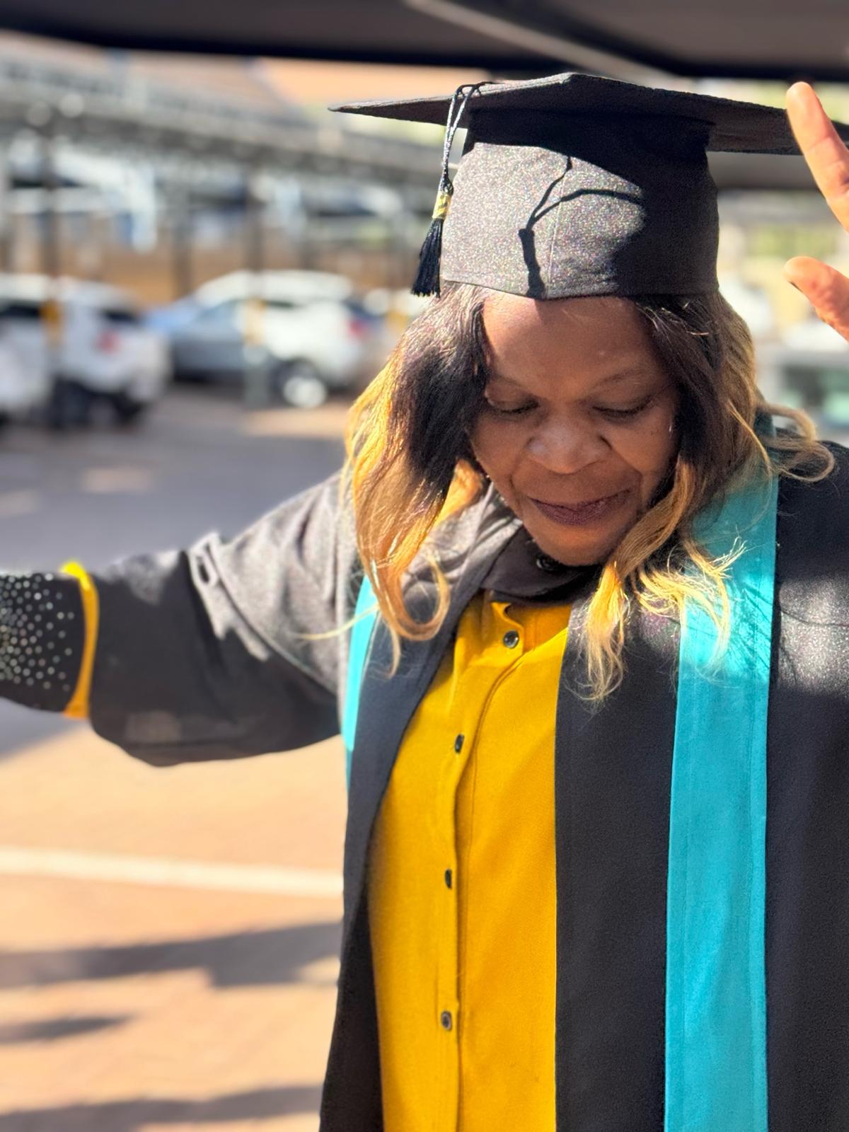 image6 Caregiver graduate in yellow dress and cap raises hands in celebration at Tuniti Care Hero graduation 2025, showcasing pride in training success