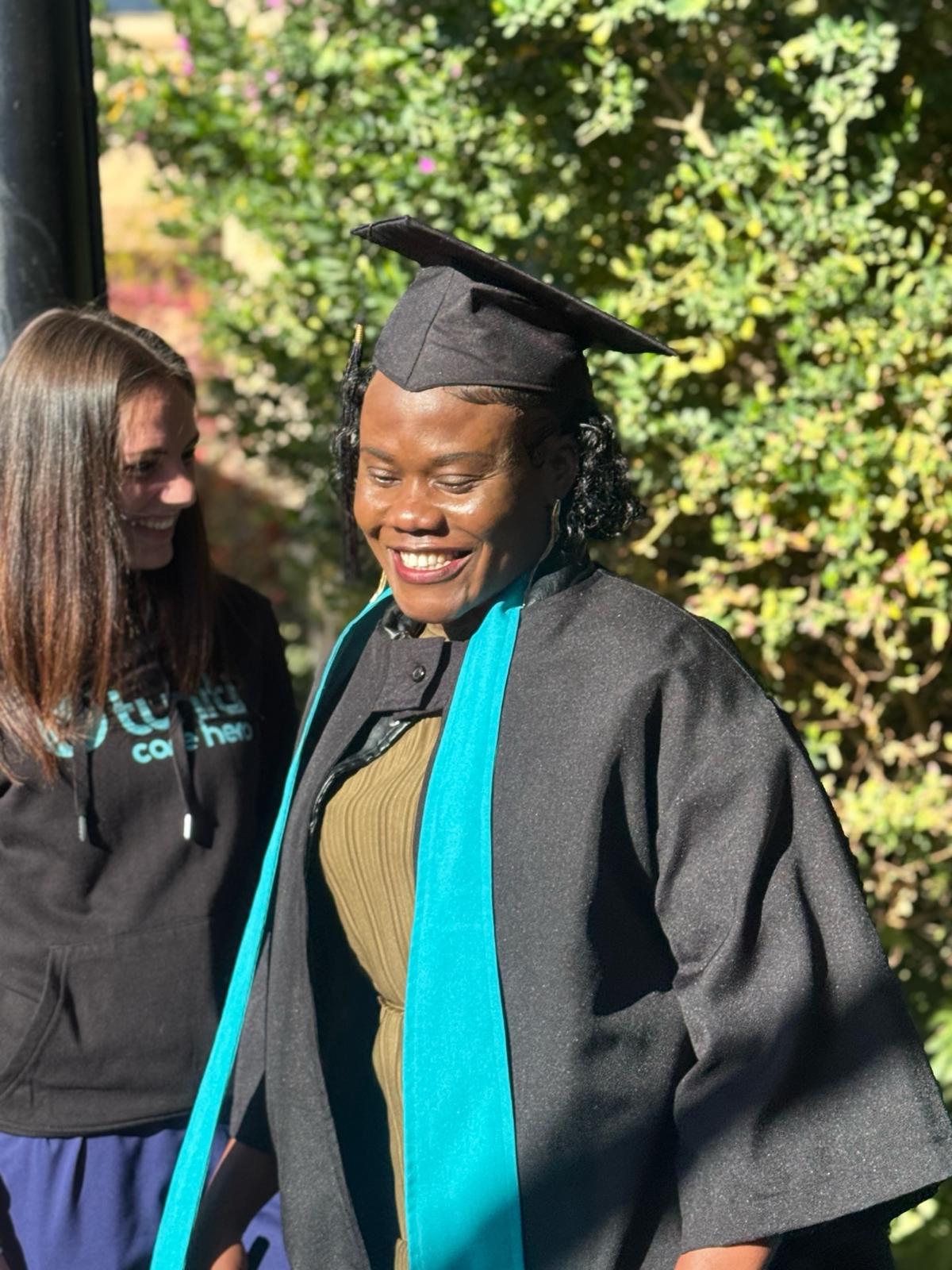 image9 Tuniti Care Hero graduate smiling in cap and gown, celebrating achievement with teammate at caregiver graduation 2025.